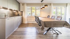 A modern kitchen with a dining area, featuring a long table and chairs, a built-in oven, and a window with a view of the outdoors. - Rapunzel Paterre B25 Appartement/Fewo, Dusche, WC, 2 Schlafräume by Interhome (Adelboden)