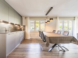 Eine moderne Küche mit Essbereich, ausgestattet mit einem langen Tisch und Stühlen, einem eingebauten Backofen und einem Fenster mit Blick ins Freie.