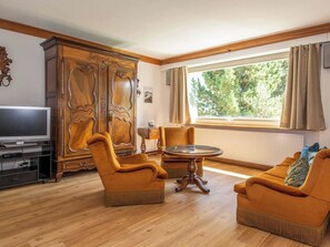 A living room with a wooden cabinet, two armchairs, a round coffee table, and a television on a stand. - Chalet Grimm Appartement/Fewo, Dusche, WC 5.5-Zimmerwohnung by Interhome (Adelboden)