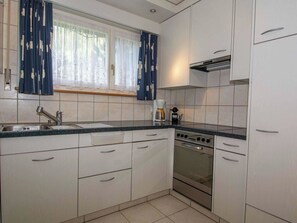A compact kitchen with white cabinets, a stainless steel sink, a coffee maker, and an oven. - Chalet Grimm Appartement/Fewo, Dusche, WC 5.5-Zimmerwohnung by Interhome (Adelboden)