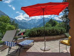 Una terraza con una sombrilla roja, dos sillones de relax y vistas a las montañas.