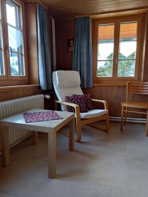A room with a wooden chair, a table, and a bench. There are windows with curtains, a radiator, and a wooden door. - Hagrösli Appartement/Fewo, Dusche, WC, 1 Schlafraum 2-Zimmerwohnung by Interhome (Adelboden)