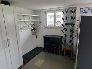 Ein kleines Zimmer mit Kleiderschrank, Schuhablage, einem kleinen Tisch und Wandfitnessgeräten.