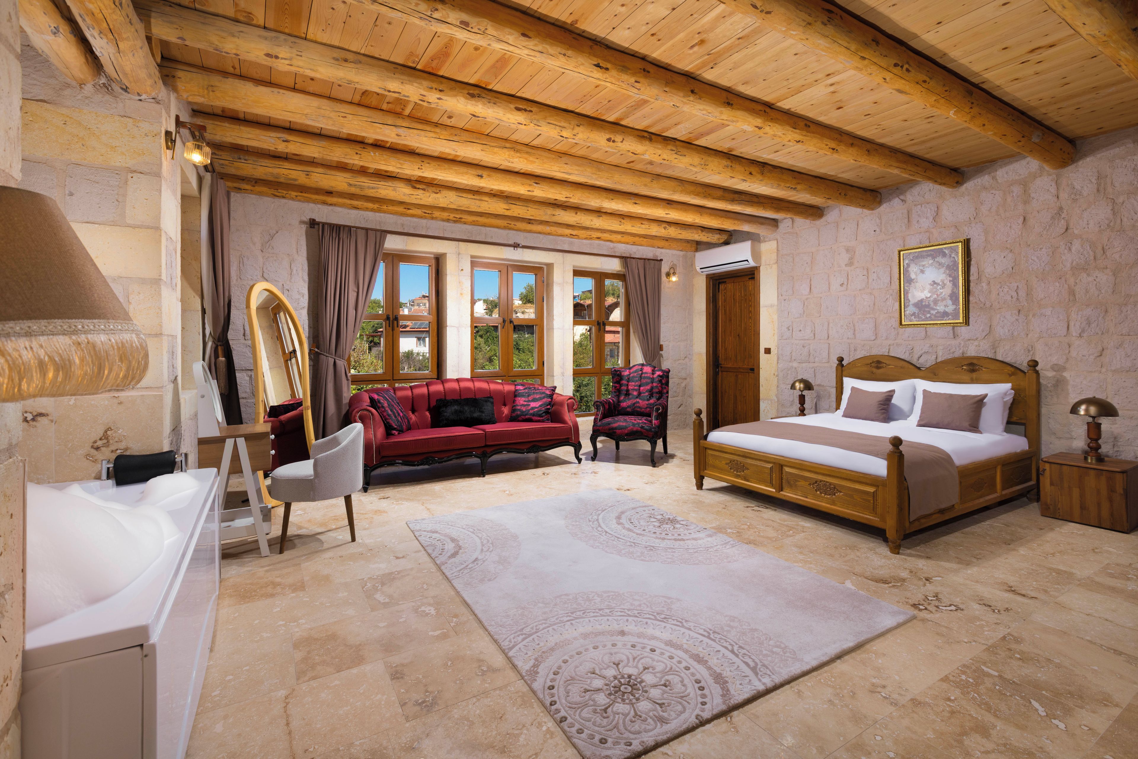 Quarto com teto de madeira, cama, sofá vermelho, cadeira, espelho e janela com vista para prédios.