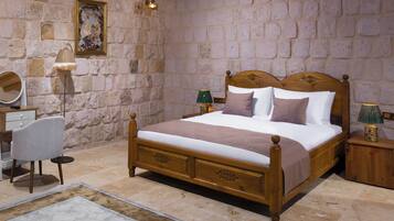 Un dormitorio con pared de piedra, una cama de madera, una mesita de noche, una lámpara, una silla y un espejo.