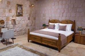 A bedroom with a stone wall, a wooden bed, a bedside table, a lamp, a chair, and a mirror. - Vespera Cappadocia (Urgup)