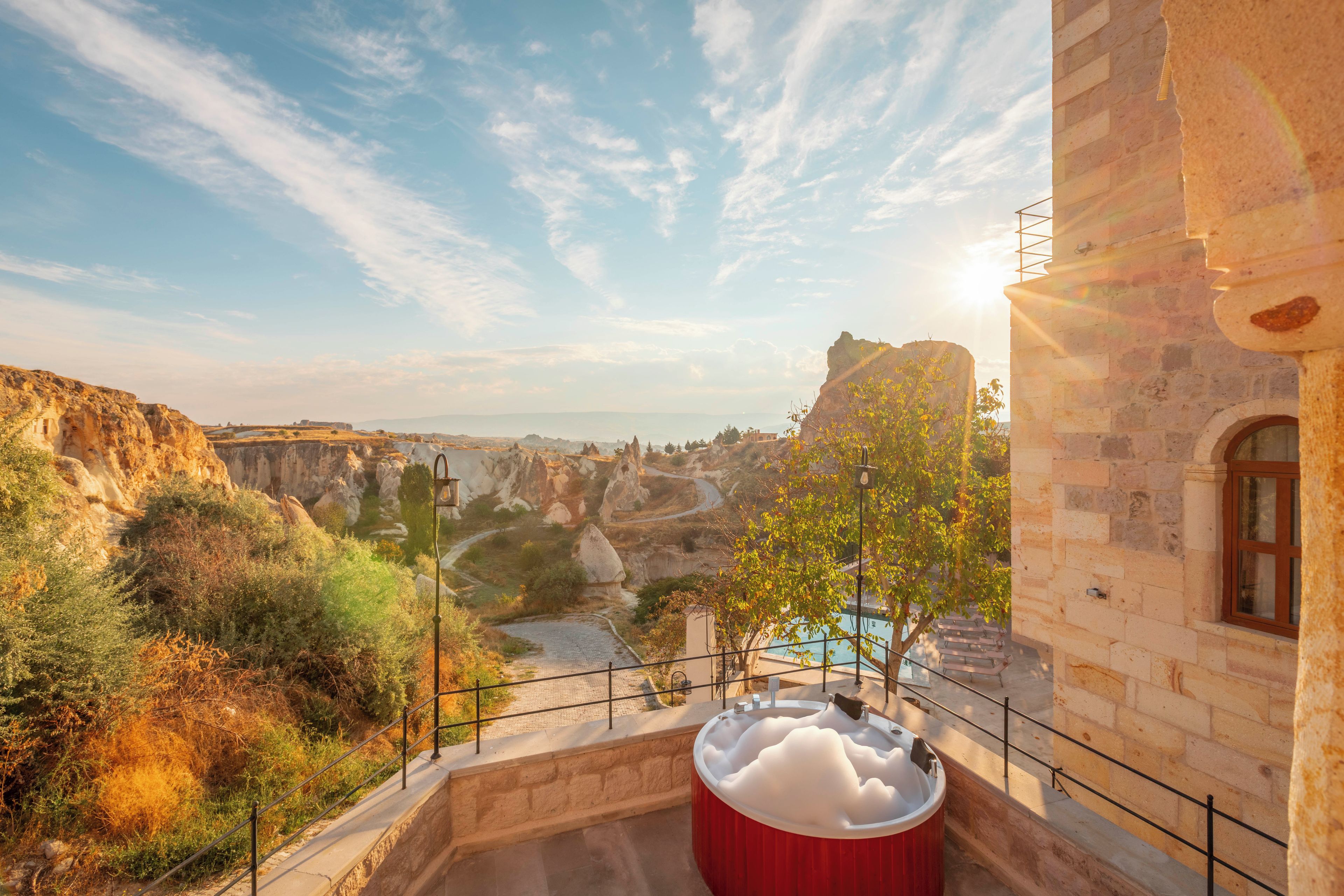 A view from a balcony overlooking a mountainous landscape with a pool and a stone building.
