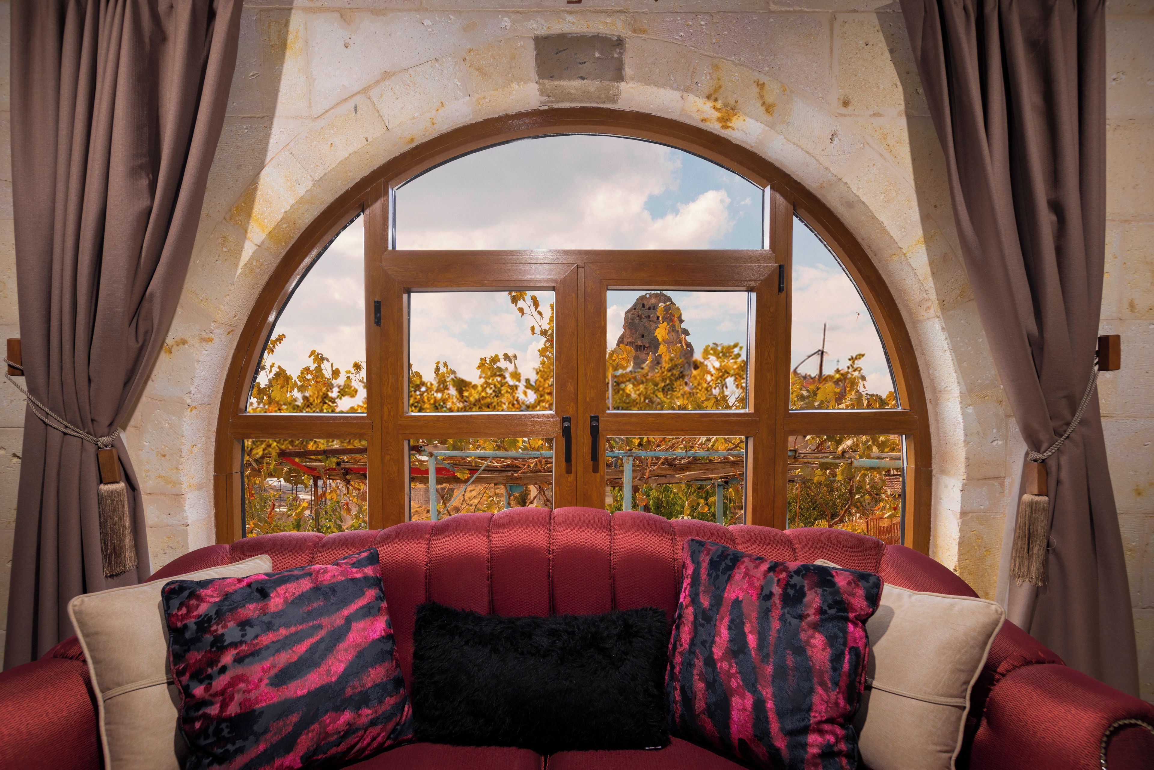 A room with a red sofa, a wooden-framed arched window, and curtains.