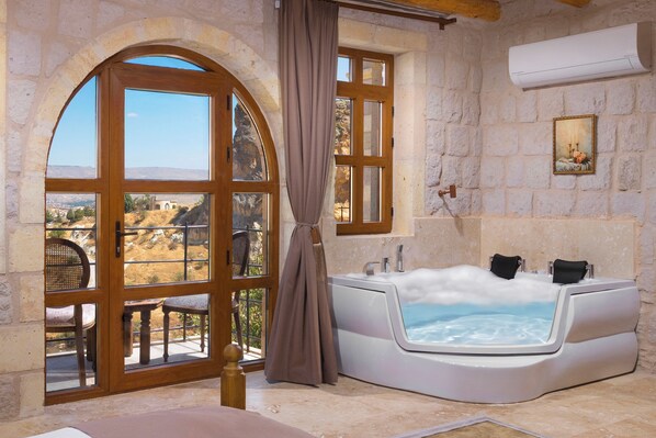 A room with a large arched doorway, a hot tub, and a view of a mountainous landscape.