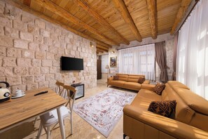 A cozy living room with a stone wall, wooden ceiling beams, a flat-screen TV, a sofa, and a coffee table.