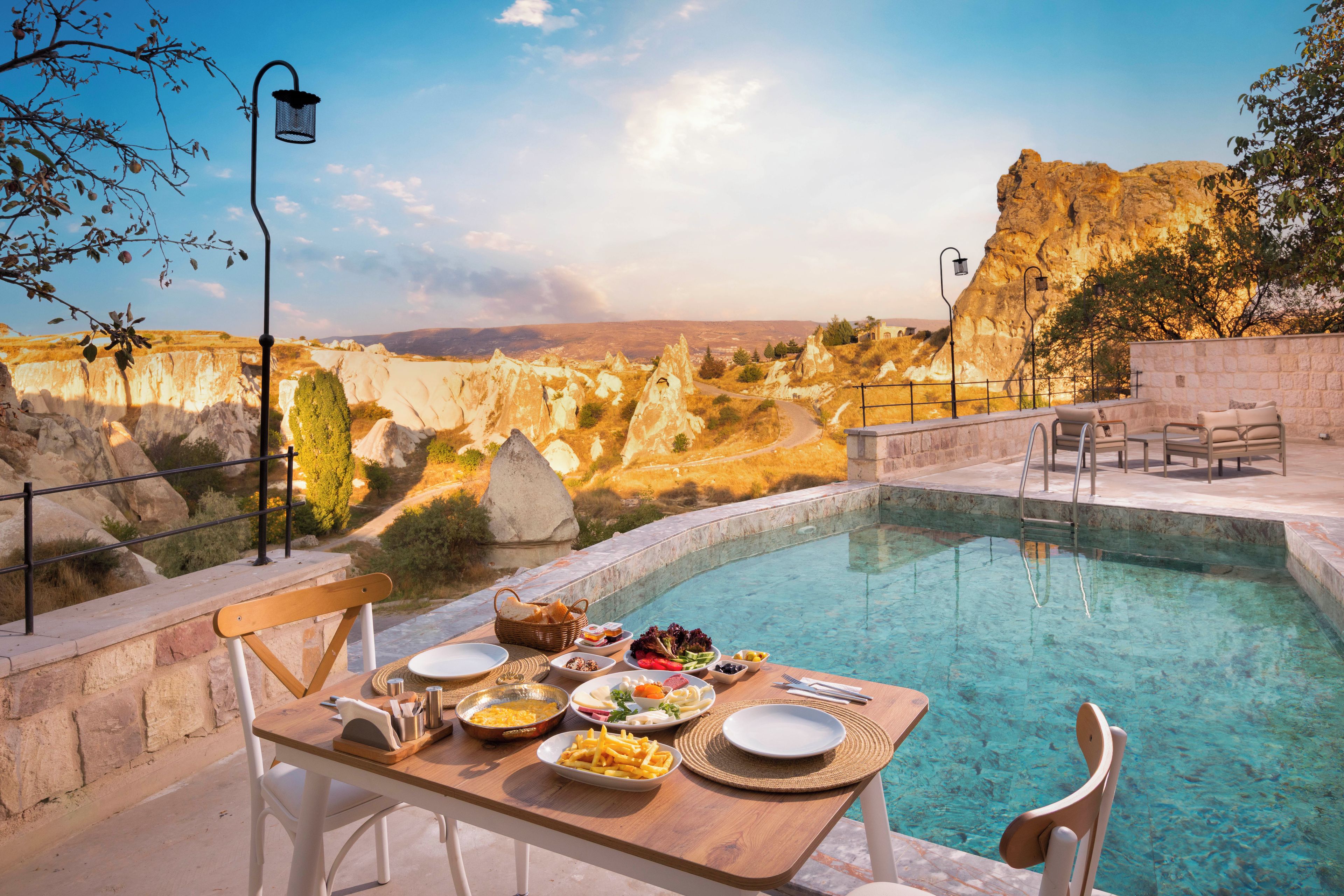 A dining table with plates of food and a clear view of a pool and rocky landscape.