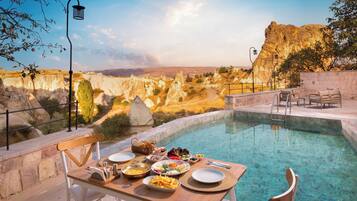 A dining table with plates of food and a clear view of a pool and rocky landscape.