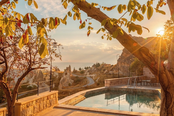 A pool area with a stone wall, a view of rocky terrain, and a clear sky.
