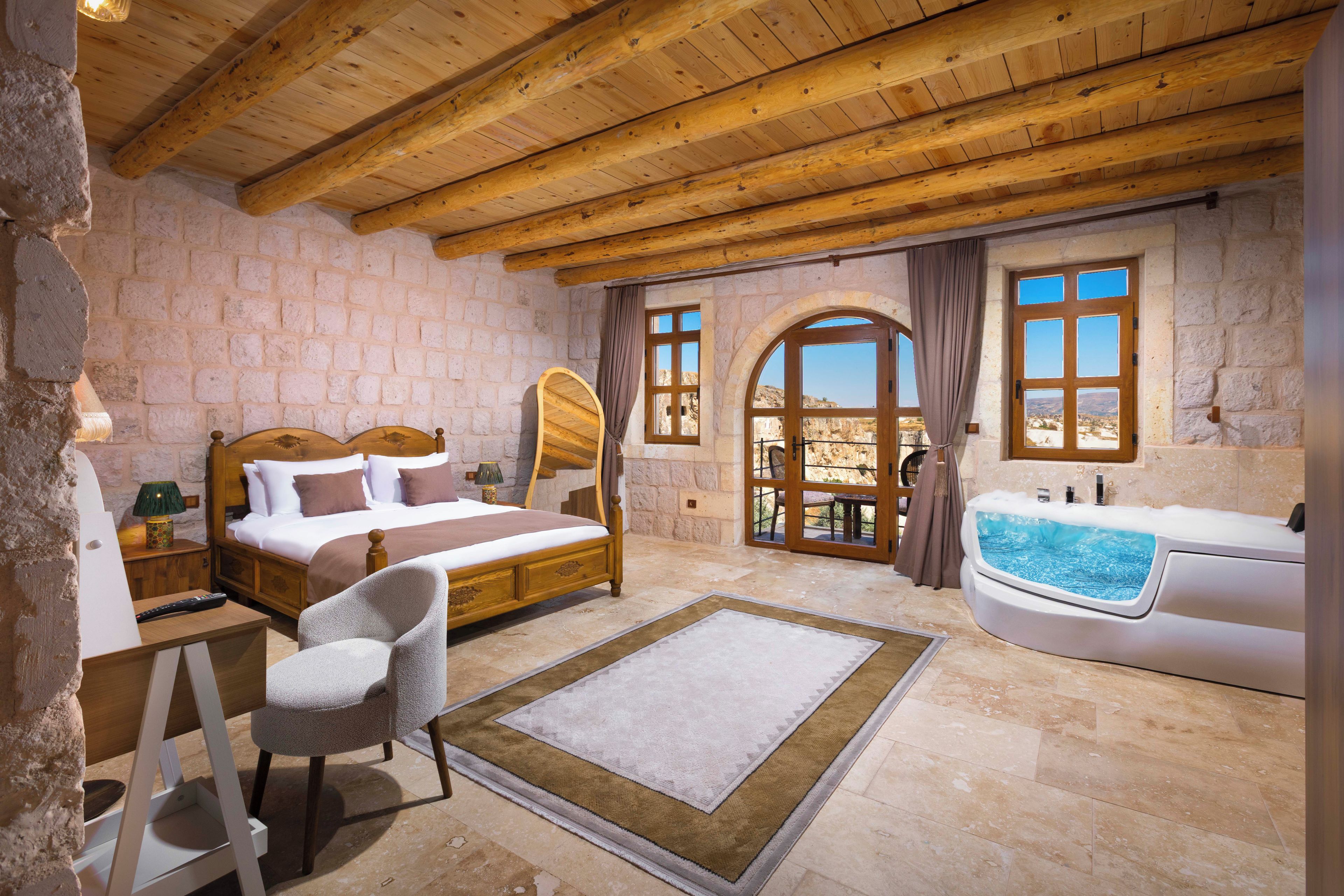 Ein Schlafzimmer mit Holzboden, Steinwänden, einem Bett, einem Sessel, einem Schreibtisch, einem Fenster und einer Badewanne.