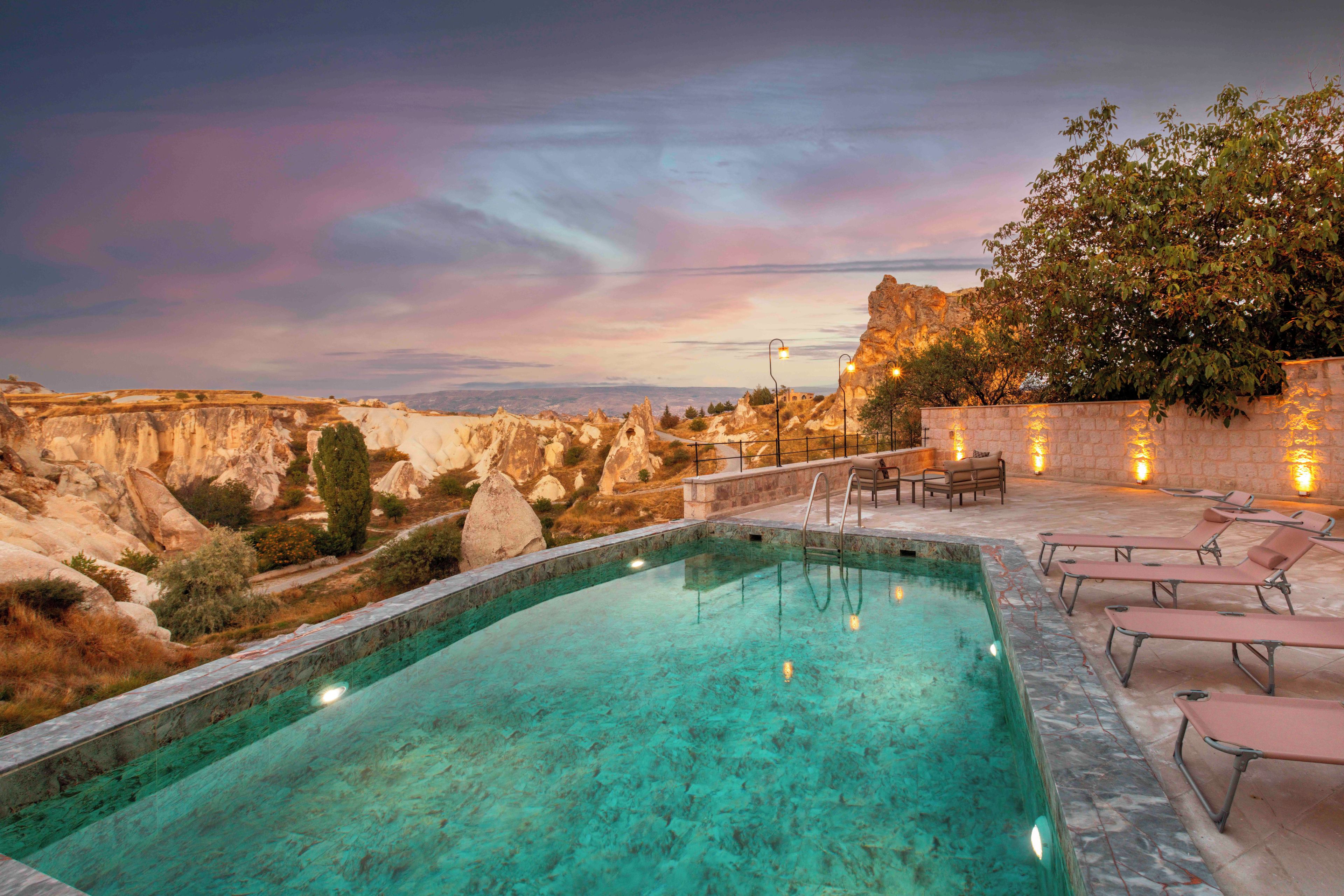 An outdoor swimming pool with clear water, surrounded by a stone wall and equipped with lounge chairs.