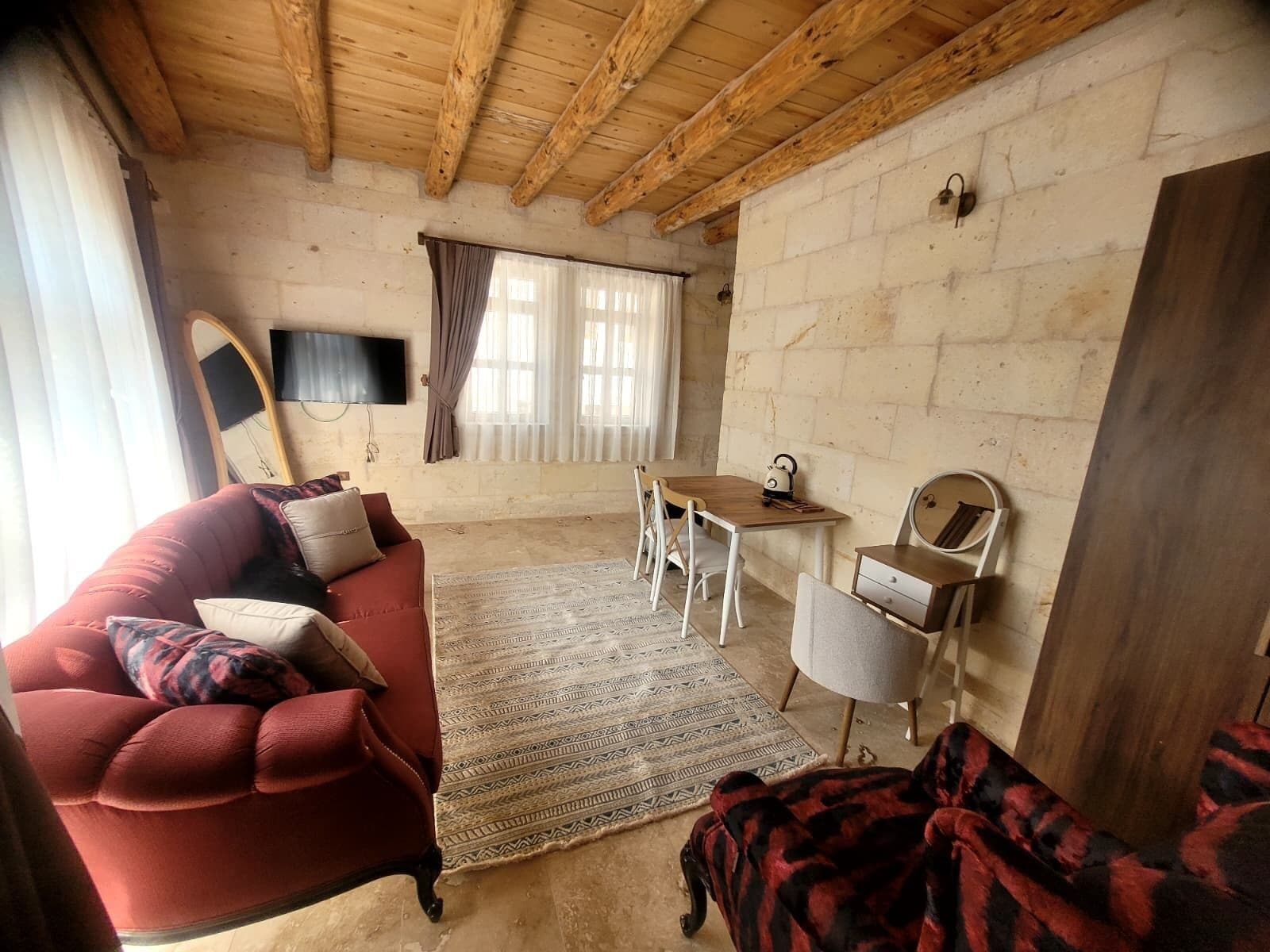Una sala de estar acogedora con un sofá rojo, un tapete estampado, una mesa de madera y un televisor montado en la pared.