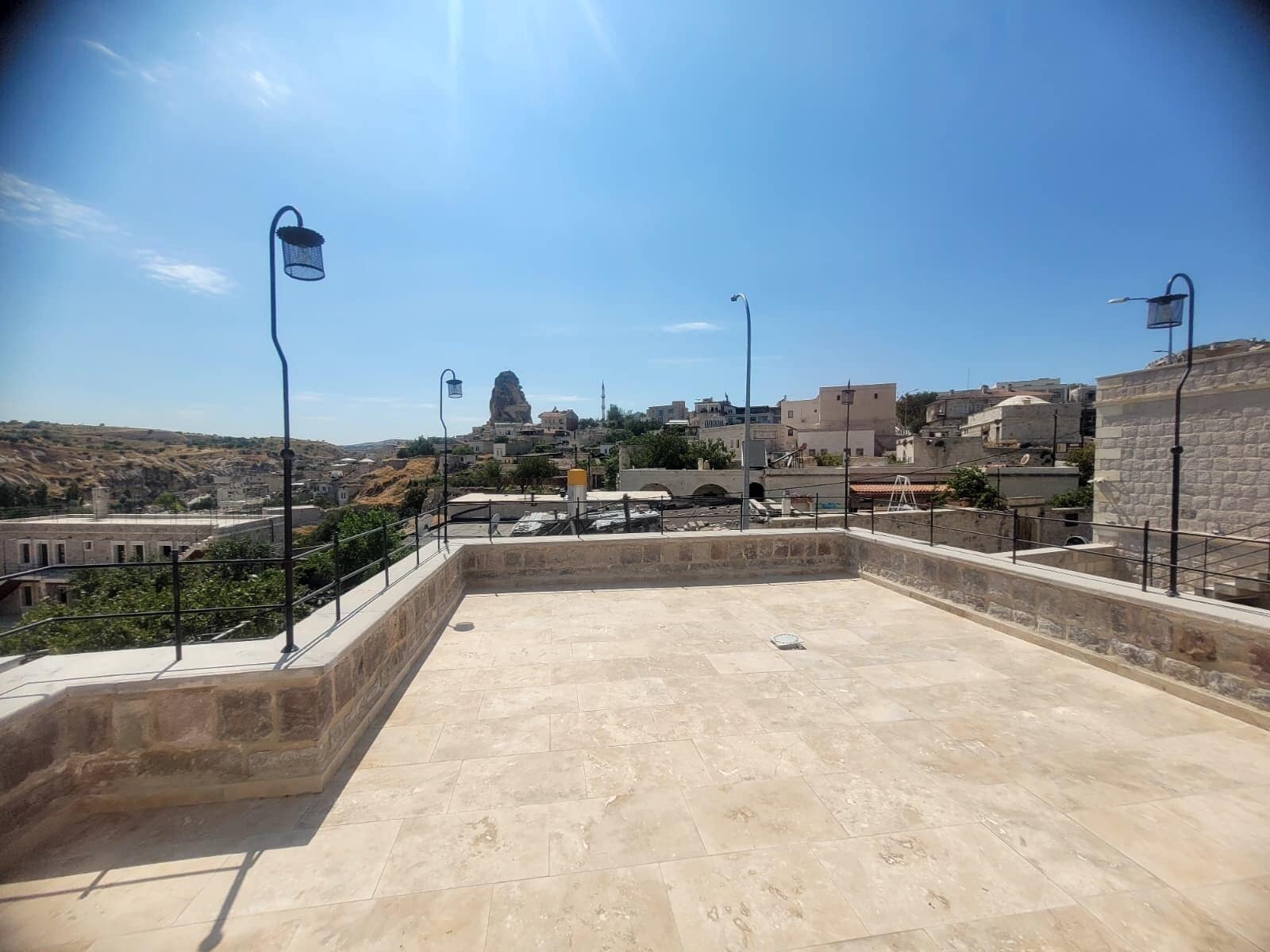 Una terraza en la azotea con suelo de piedra, barandillas metálicas y farolas.