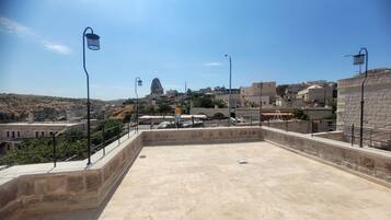 Una terraza en la azotea con suelo de piedra, barandillas metálicas y farolas.