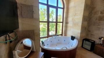 Un baño con un amplio ventanal de arco, una bañera, un espejo y un televisor.
