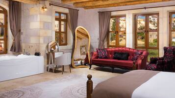Una habitación con una cama grande, un sofá rojo, un espejo con marco de madera, una bañera blanca y paredes de piedra.
