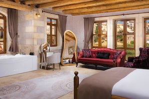 Una habitación con una cama grande, un sofá rojo, un espejo con marco de madera, una bañera blanca y paredes de piedra.