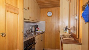 A compact kitchen with wooden cabinets, a stove, and a clock on the wall. - Chalet Iris Appartement/Fewo, Dusche, WC, 2 Schlafräume 3-Zimmerwohnung by Interhome (Adelboden)
