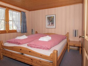 A wooden bed with checkered bedding, a bedside table, a nightstand, a window with curtains, and a framed picture on the wall. - Chalet Iris Appartement/Fewo, Dusche, WC, 2 Schlafräume 3-Zimmerwohnung by Interhome (Adelboden)