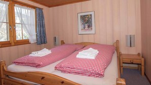 A room with a wooden bed, a window with curtains, a framed picture on the wall, and a small bedside table. - Chalet Iris Appartement/Fewo, Dusche, WC, 2 Schlafräume 3-Zimmerwohnung by Interhome (Adelboden)