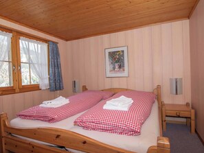 Ein Zimmer mit einem hölzernen Bett, einem fenster mit Vorhängen, einem gerahmten Bild an der Wand und einem kleinen Nachttisch.