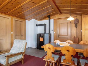 Een houten interieur met een eettafel, stoelen, een open haard en een klok aan de muur.