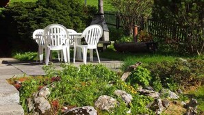 An outdoor seating area with white chairs and a table, surrounded by a garden with rocks and plants. - Chalet Iris Appartement/Fewo, Dusche, WC, 2 Schlafräume 3-Zimmerwohnung by Interhome (Adelboden)