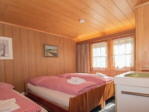 Una habitación de cabaña de madera con una cama, una mesita y un ventanal con cortinas.