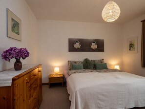 A bedroom with a bed, two bedside lamps, a wooden dresser, a vase of flowers, and wall art. - Chalet Delphin Appartement/Fewo, Bad, WC, 1 Schlafraum 2-Zimmerwohnung by Interhome (Adelboden)