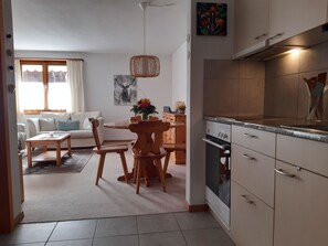 A modern kitchen with white cabinets, a built-in oven, and a dining area with a wooden table and chairs. - Chalet Delphin Appartement/Fewo, Bad, WC, 1 Schlafraum 2-Zimmerwohnung by Interhome (Adelboden)