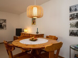 A dining area with a round wooden table, chairs, a woven pendant light, a candle, and wall-mounted photographs. - Chalet Delphin Appartement/Fewo, Bad, WC, 1 Schlafraum 2-Zimmerwohnung by Interhome (Adelboden)