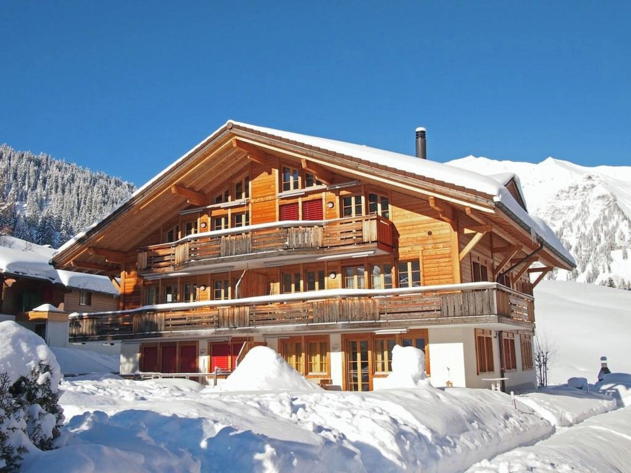 Eine mehrstöckige Holzchalet mit Balkonen, eingebettet in eine verschneite Berglandschaft.