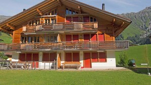 Un'ampia chalet in legno con numerosi balconi, una zona relax esterna coperta e uno sfondo montuoso.