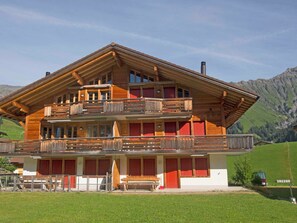 Eine große Holzhütte mit mehreren Balkonen, einer überdachten Außenveranda und einer Bergkulisse im Hintergrund.