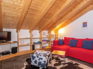 A cozy living room with a red sofa, wooden bookshelves, a television, and a cow-print ottoman. - Am Gilsbach 1 Appartement/Fewo, Dusche und Bad, WC, 3 Schlafräume by Interhome (Adelboden)