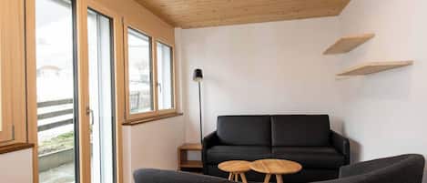 A modern living room with a black sofa, two black armchairs, a wooden floor, and a ceiling light fixture.