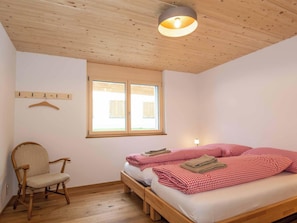 A room with a wooden ceiling, a bed with red and white checkered bedding, a chair, and a window with shutters. - Chalet Sonne Appartement/Fewo, Dusche, WC, 2 Schlafräume 3-Zimmerwohnung by Interhome (Adelboden)