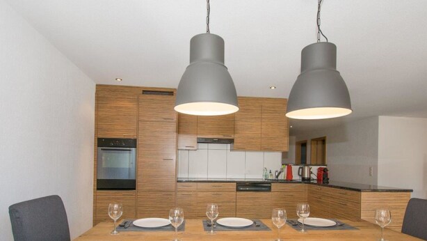 A modern kitchen with wooden cabinets, a built-in oven, and a dining table set for six with glasses and cutlery. - Schützenrain 1. Stock Appartement/Fewo, Bad, WC, 3 Schlafräume by Interhome (Adelboden)