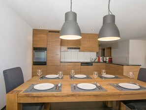Une cuisine moderne avec des meubles en bois, un four encastré et une table à manger pour six personnes, agrémentée de verres et de couverts.