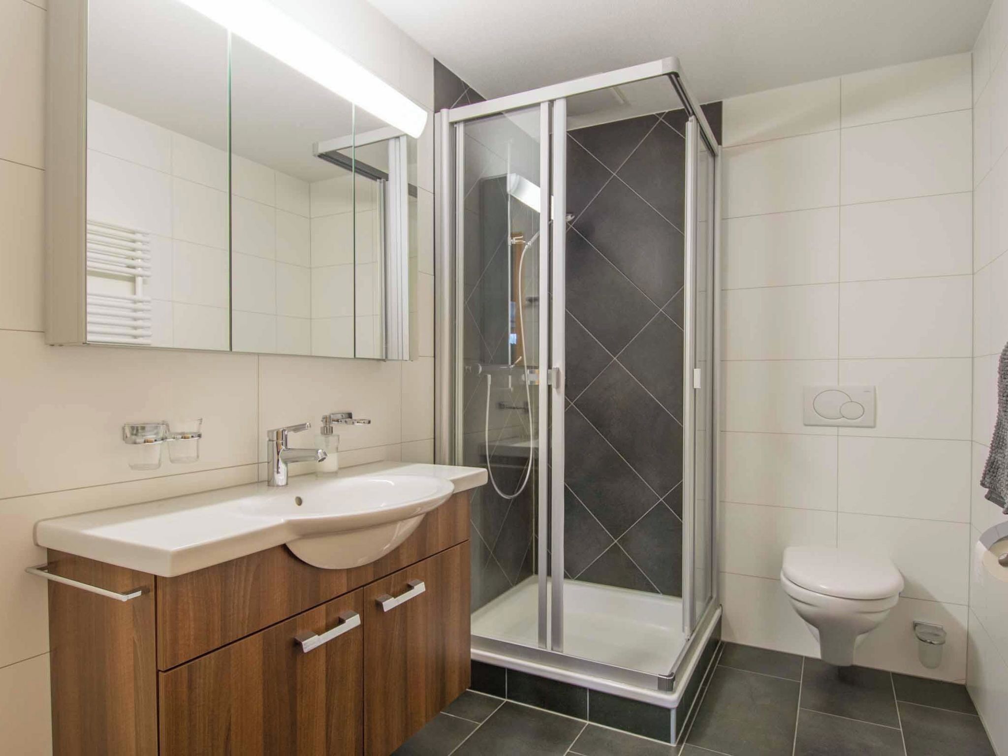 A modern bathroom with a glass shower enclosure, a wooden vanity with a sink, and a toilet.
