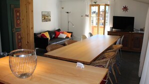 A dining area with a wooden table and chairs, a television, and a sofa in the background. - Haus Baumann Appartement/Fewo, Bad, WC, 4 oder mehr Schlafräume 5 Zimmerwohnung by Interhome (Adelboden)