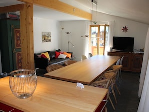 A dining area with a wooden table and chairs, a television, and a sofa in the background. - Haus Baumann Appartement/Fewo, Bad, WC, 4 oder mehr Schlafräume 5 Zimmerwohnung by Interhome (Adelboden)