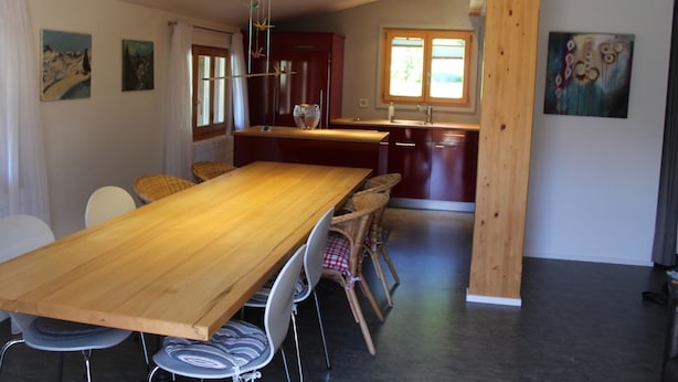 A spacious dining area with a long wooden table and wicker chairs, a kitchen with wooden cabinets, and a window providing natural light. - Haus Baumann Appartement/Fewo, Bad, WC, 4 oder mehr Schlafräume 5 Zimmerwohnung by Interhome (Adelboden)