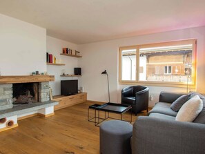 A living room with a fireplace, a television, a sofa, and a window with a view of a wooden building. - Titschermatte Appartement/Fewo, Bad, WC, 2 Schlafräume 3-Zimmerwohnung by Interhome (Adelboden)