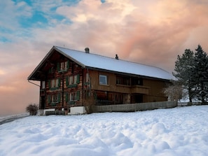 Eine Holzhütte mit schneebedecktem Dach, umgeben von Schnee, und einem klaren Himmel.