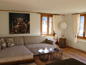 Un salon avec un canapé, deux petites tables, un tableau et une fenêtre avec des rideaux.